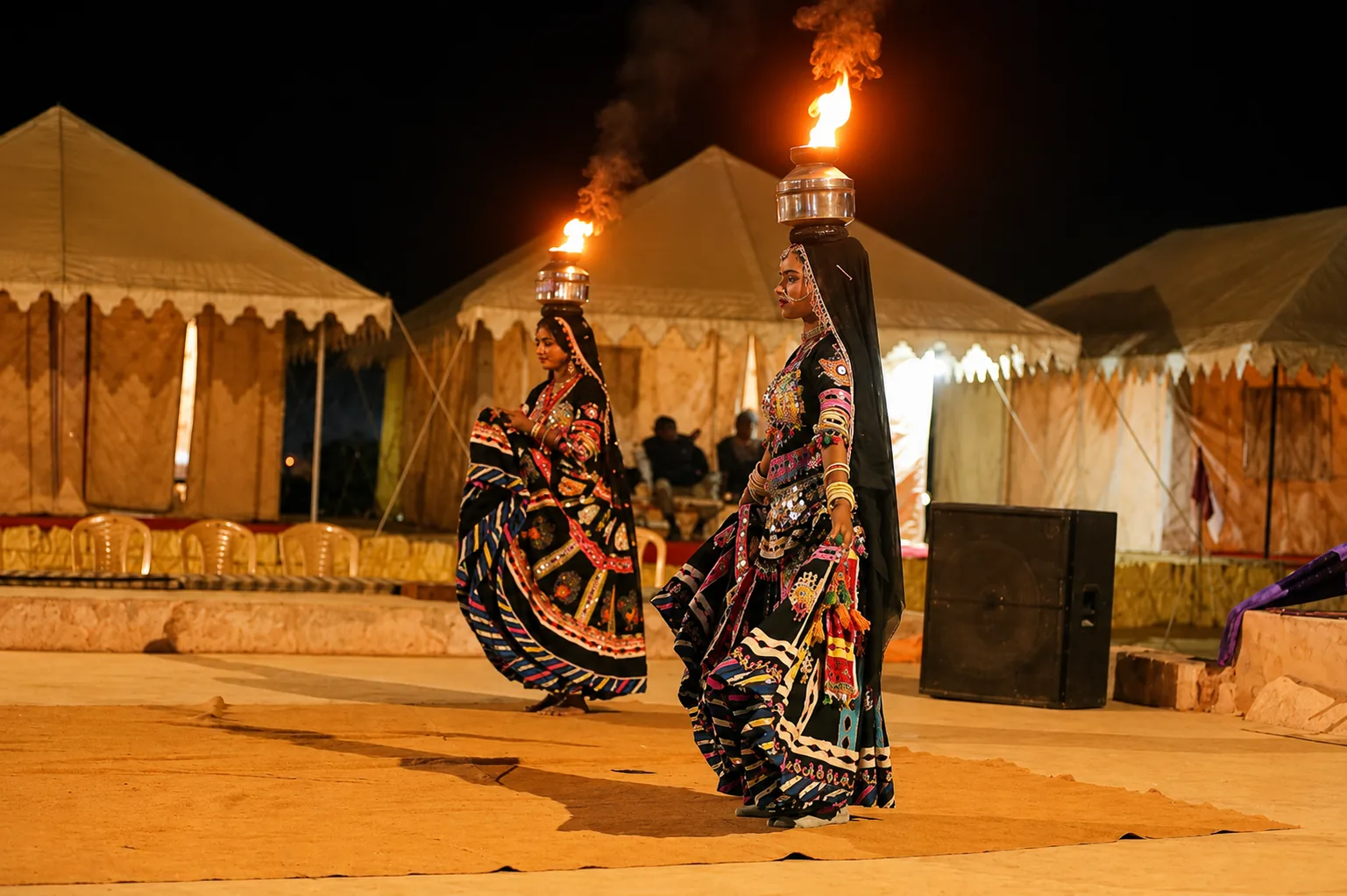 Traditional Rajasthani fire dancers performing at Melody Moon Desert Camp at night, with luxury tents in the background